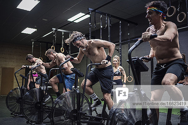 Männer  die auf einem Fitnessrad trainieren  mit Frauen  die im Hintergrund im Fitnessstudio stehen