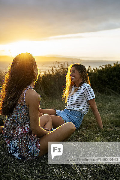 Lächelnde junge Frau verbringt ihre Freizeit mit einem Freund auf einem Feld bei Sonnenuntergang