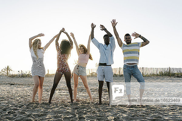 Freunde mit erhobener Hand am Strand stehend an einem sonnigen Tag