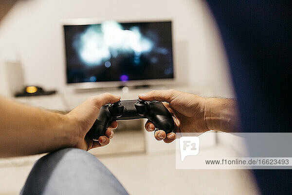 Hände eines jungen männlichen Gamers  der einen Controller hält  während er zu Hause spielt