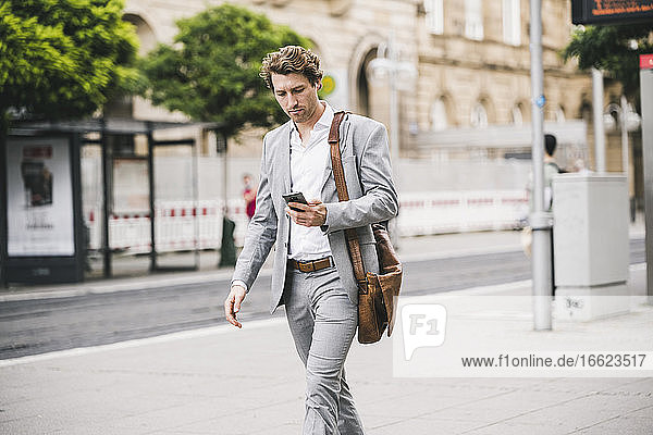 Businessman using mobile phone while walking in city