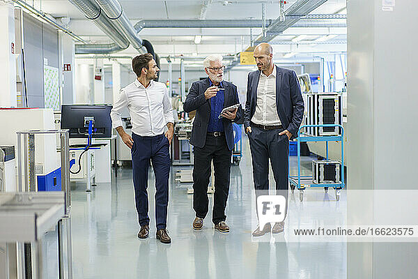 Senior manager with colleagues discussing over digital tablet while walking at illuminated factory