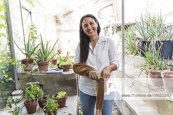 Lächelnde reife Frau  die einen Gartenhandschuh trägt  während sie im Gartenschuppen steht