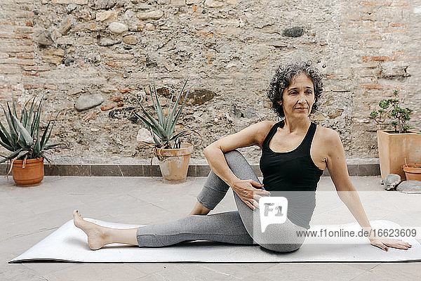 Flexible reife Frau übt Yoga auf einer Übungsmatte im Hinterhof