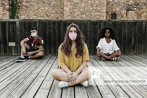 Freunde tragen einen Gesichtsschutz  während sie während des Covid-19 auf dem Holzboden sitzen
