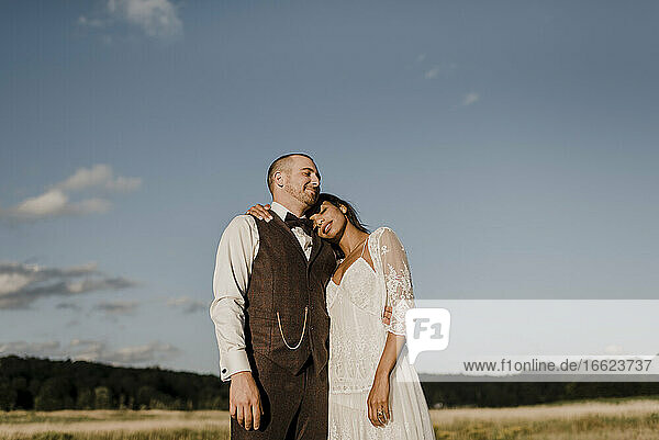 Bride leaning on bridegroom's shoulder while standing at field