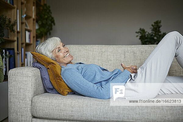 Lächelnde ältere Frau  die zu Hause auf dem Sofa liegt
