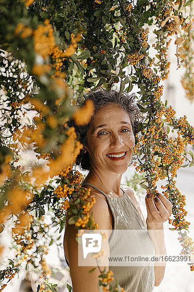 Reife Frau berührt Orangenbaum an einem sonnigen Tag