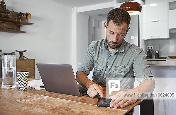 Confident mid adult businessman using smart phone while working at home