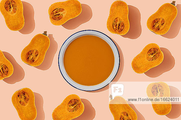 Studio shot of bowl of pumpkin soup surrounded by halves of butternut squash