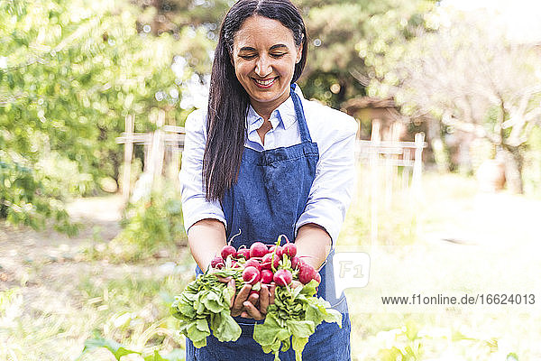Glückliche Frau zeigt frisch geerntete Bio-Radieschen aus dem Garten