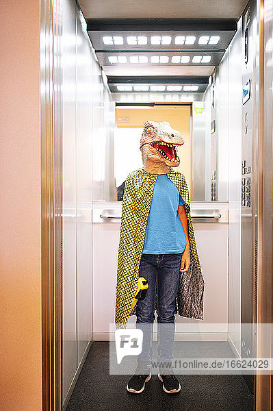 Boy wearing dinosaur mask and cape standing in elevator