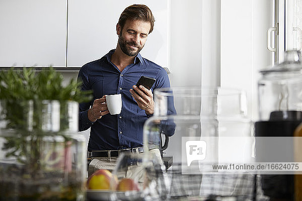 Geschäftsmann  der ein Mobiltelefon benutzt  während er in einer Cafeteria Kaffee trinkt