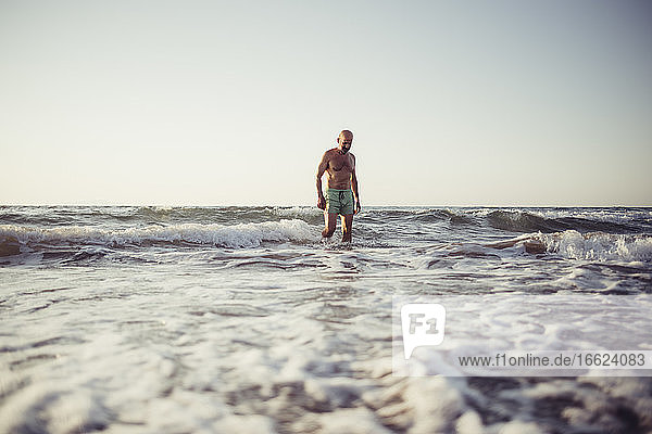 Mann geht bei Sonnenuntergang am Strand im Wasser spazieren