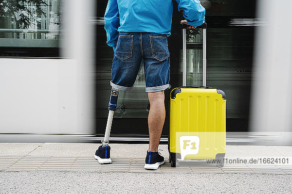 Junger Mann mit Bein- und Fußprothese steht neben Gepäckstücken auf dem Bahnhof