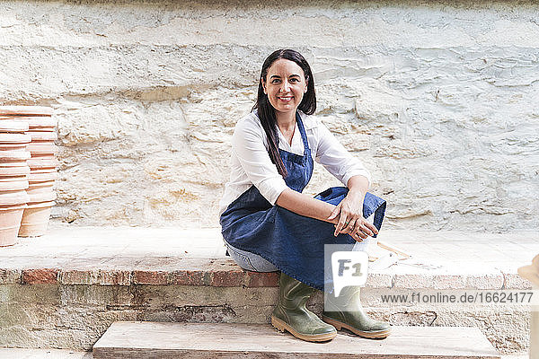 Lächelnde Frau im Gartenhaus an der Wand sitzend an einem sonnigen Tag
