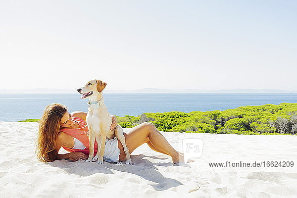 Frau mit Hund entspannt am Strand gegen den klaren Himmel an einem sonnigen Tag