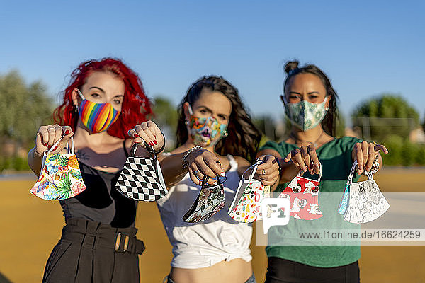 Friends holding multi colored face mask while standing outdoors