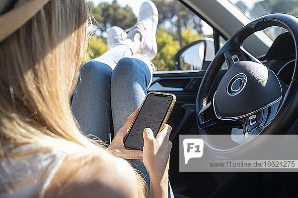 Junge Frau  die im Auto sitzend ein Mobiltelefon benutzt