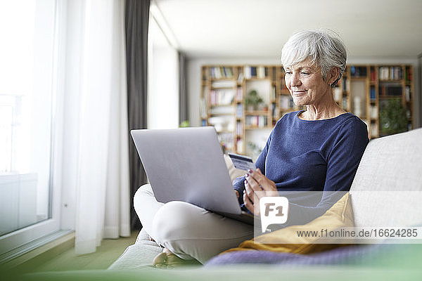 Ältere Frau benutzt Kreditkarte beim Online-Einkauf auf dem Laptop zu Hause