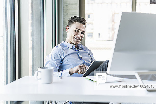 Lächelnder Geschäftsmann mit digitalem Tablet am Schreibtisch im Büro