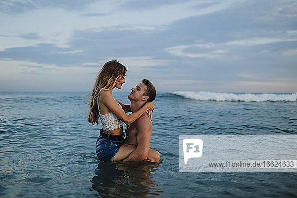 Freund trägt Freundin im Wasser stehend am Strand