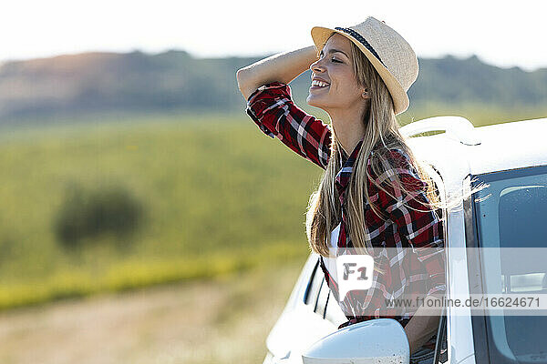 Schöne Frau mit Hut  die sich lächelnd aus dem Autofenster lehnt