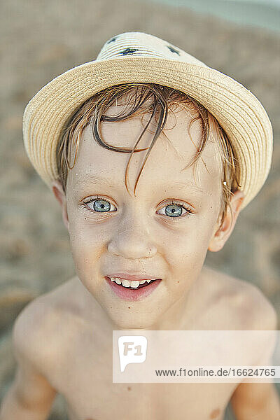 Lächelnder Junge mit Hut am Strand stehend