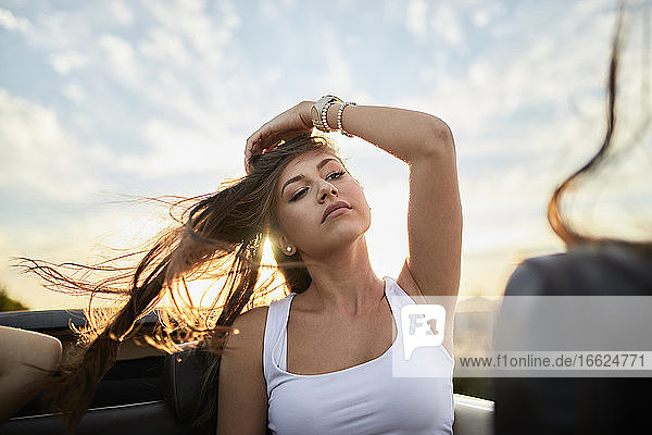 Junge Frau schaut weg  während sie in einem Cabrio gegen den Himmel bei Sonnenuntergang sitzt
