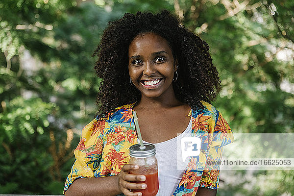 Smiling young woman holding juice while standing in park
