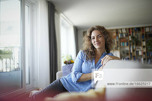 Smiling woman sitting on sofa by window at home