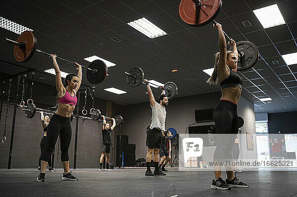 Athletes lifting barbell while exercising in gym