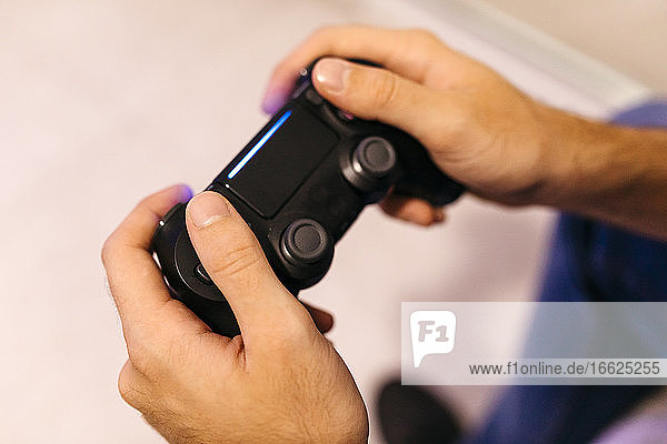 Hände eines jungen Mannes  der einen Controller hält  während er zu Hause ein Videospiel spielt