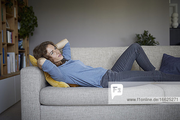 Mid adult woman with head in hands lying on sofa at home