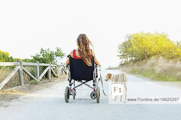 Frau im Rollstuhl mit Hund auf Straße gegen klaren Himmel