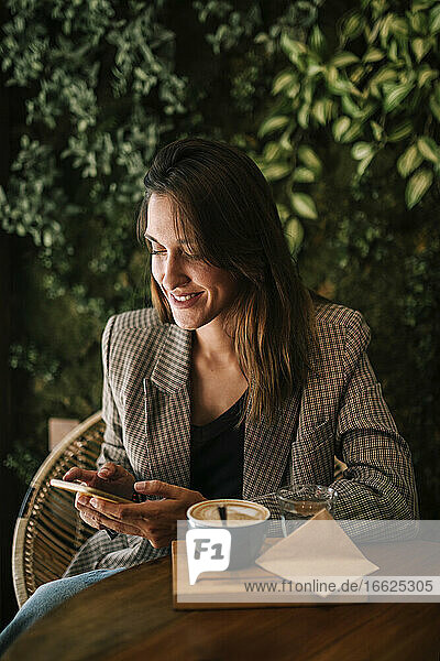 Junge Frau  die in einem Café sitzt und mit ihrem Smartphone SMS schreibt