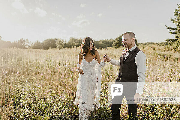 Paar hält sich an der Hand und geht in einem Feld an einem sonnigen Tag