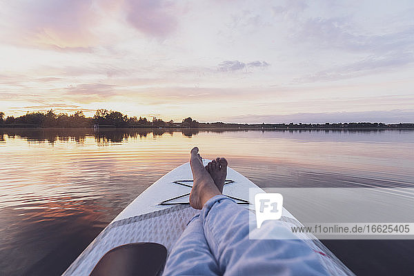Beine einer Frau  die sich bei Sonnenuntergang auf einem Paddleboard entspannt