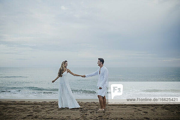 Paar hält sich an den Händen und tanzt gegen das Meer am Strand