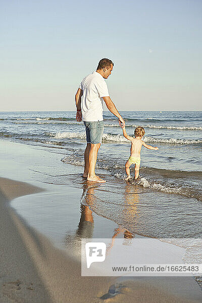 Junge hält die Hand seines Vaters beim Spielen im Wasser am Strand