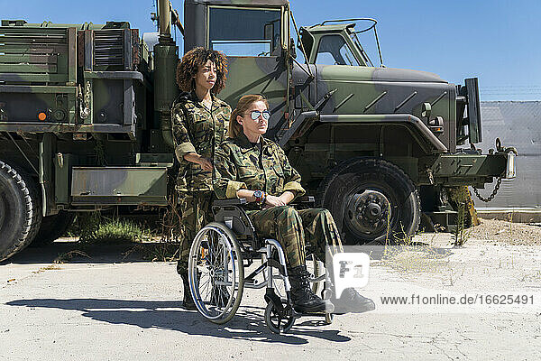 Junge Soldatin mit behindertem Kollegen im Rollstuhl vor einem Lastwagen auf einem Armeestützpunkt an einem sonnigen Tag