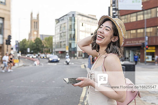 Woman laughing while using smart phone standing on street in city
