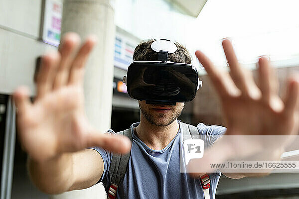 Young man gesturing while enjoying virtual reality headset at subway station