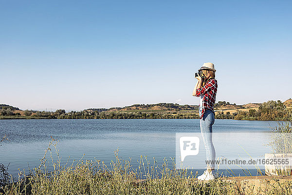 Woman taking photo with camera while standing on steps at lake