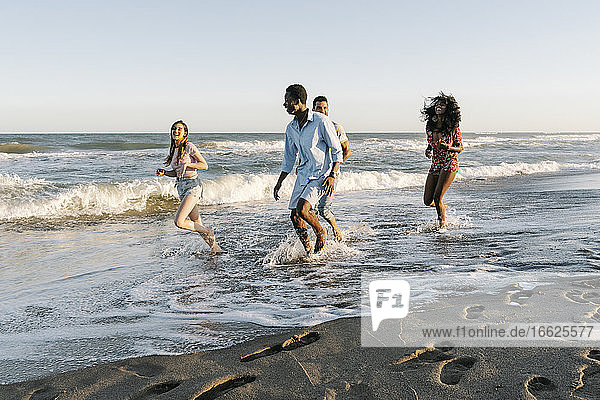 Young friends enjoying while walking on beach during sunny day