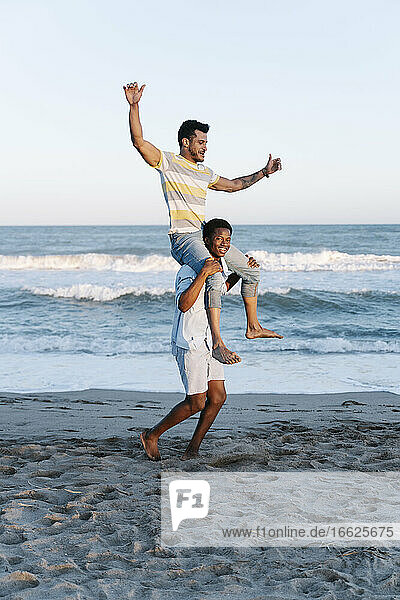 Young man carrying friend on shoulder at beach