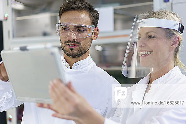 Männliche und weibliche Techniker diskutieren über einem digitalen Tablet in einem beleuchteten Labor