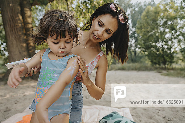 Mutter trägt Sonnenschutzmittel auf ihre Tochter am Strand auf