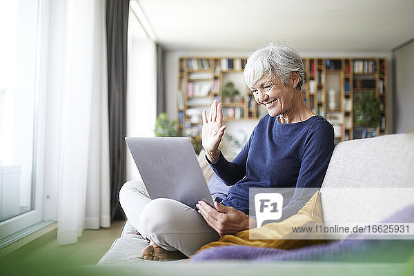 Ältere Frau macht High Five bei einem Videoanruf  während sie einen Laptop zu Hause benutzt