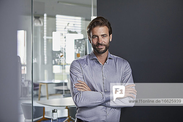Confident businessman with arms crossed standing in office